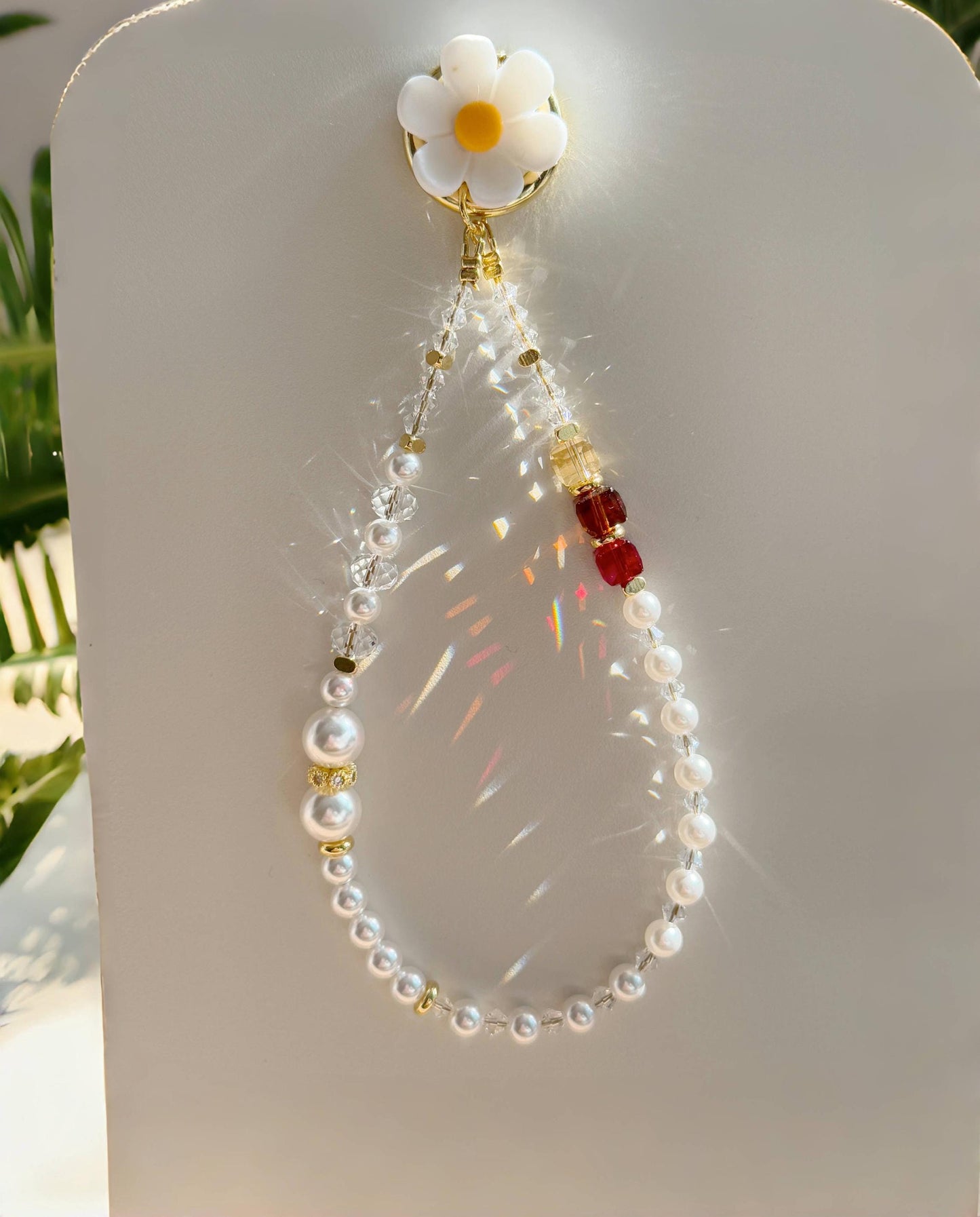 This phone charm features a delicate blend of pearls and sparkling crystal beads. The design is enhanced with gold-tone accents, including small golden spacers and a charming daisy-shaped clip at the top