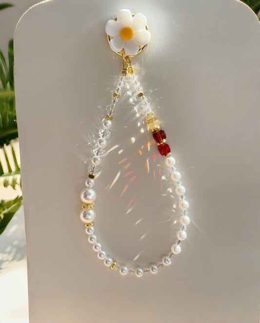 This phone charm features a delicate blend of pearls and sparkling crystal beads. The design is enhanced with gold-tone accents, including small golden spacers and a charming daisy-shaped clip at the top